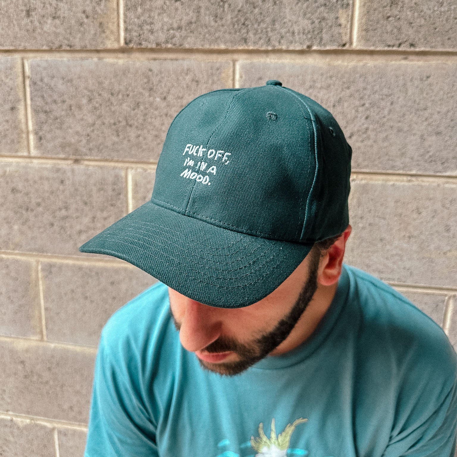 Urban streetwear image of bearded man wearing a dark green dad cap style Fuck Off hat.