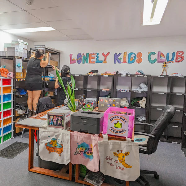 A candid warehouse photo of Two team members at the Lonely Kids Club studio in Sydney, packing orders. There is Lonely Kids Club colourful branding around them.