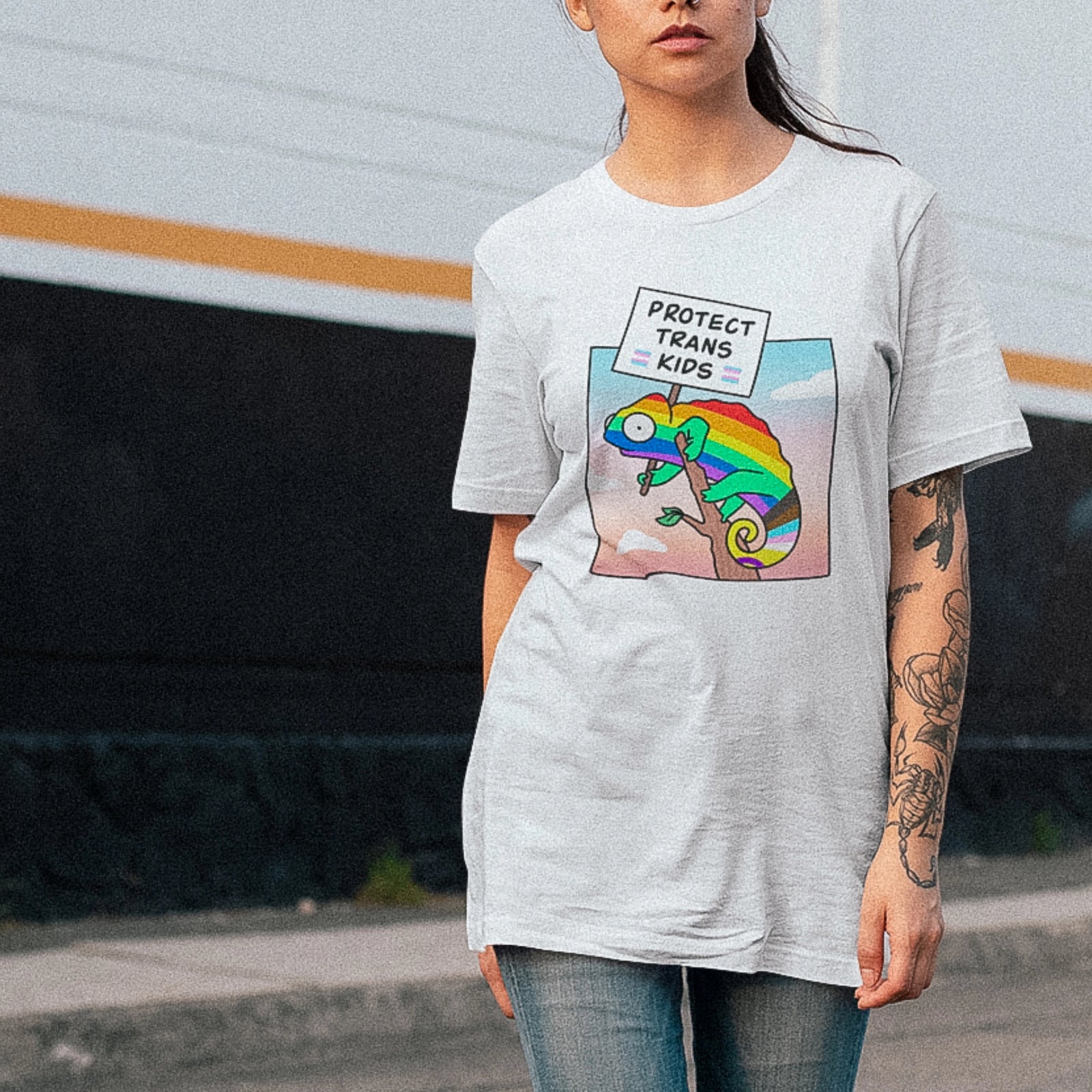 Person wearing a t-shirt with a rainbow chameleon graphic and 'Protect Trans Kids' text.